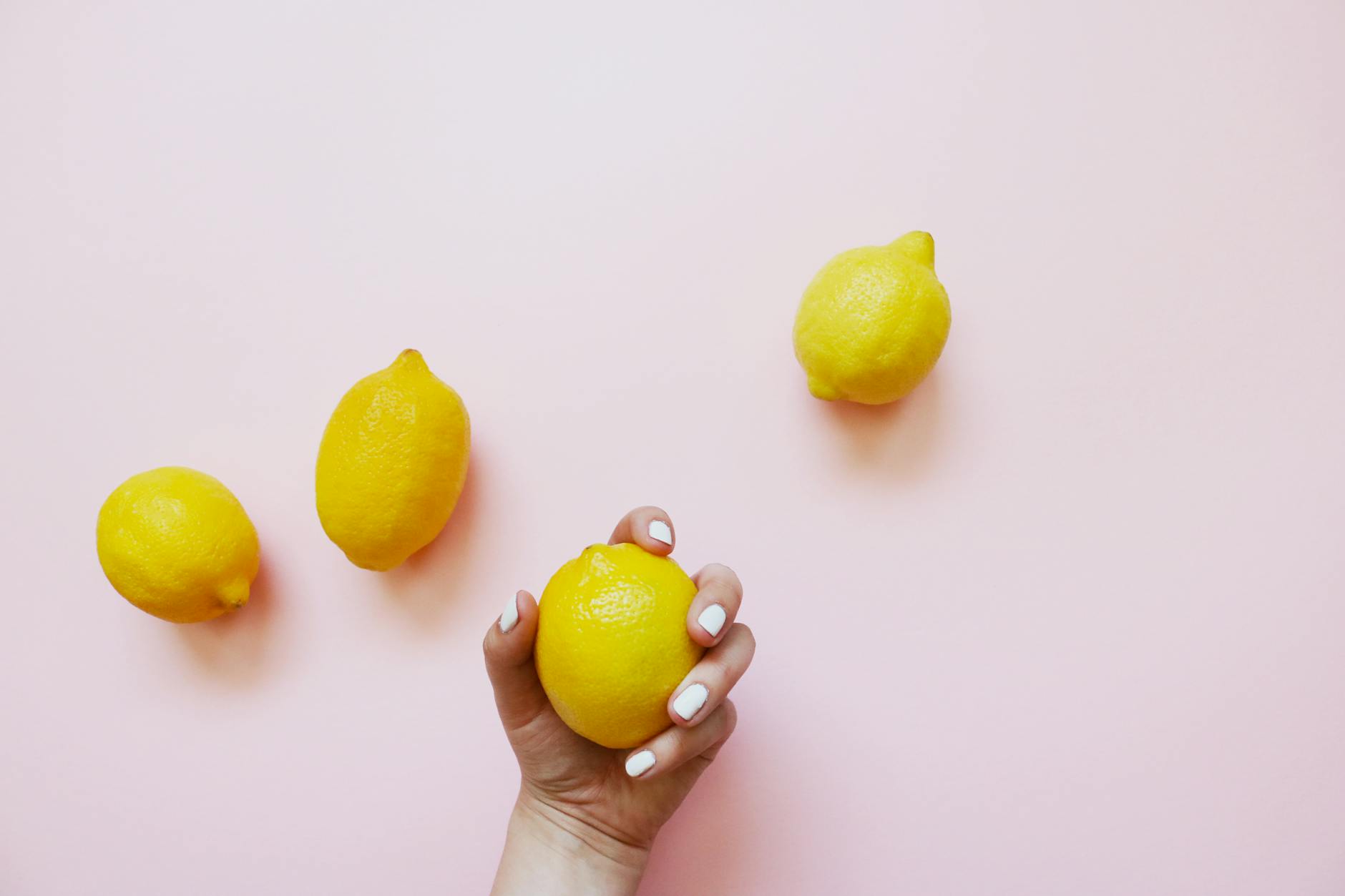 A hand holding a lemon on a soft pink background, symbolizing refreshing intimacy