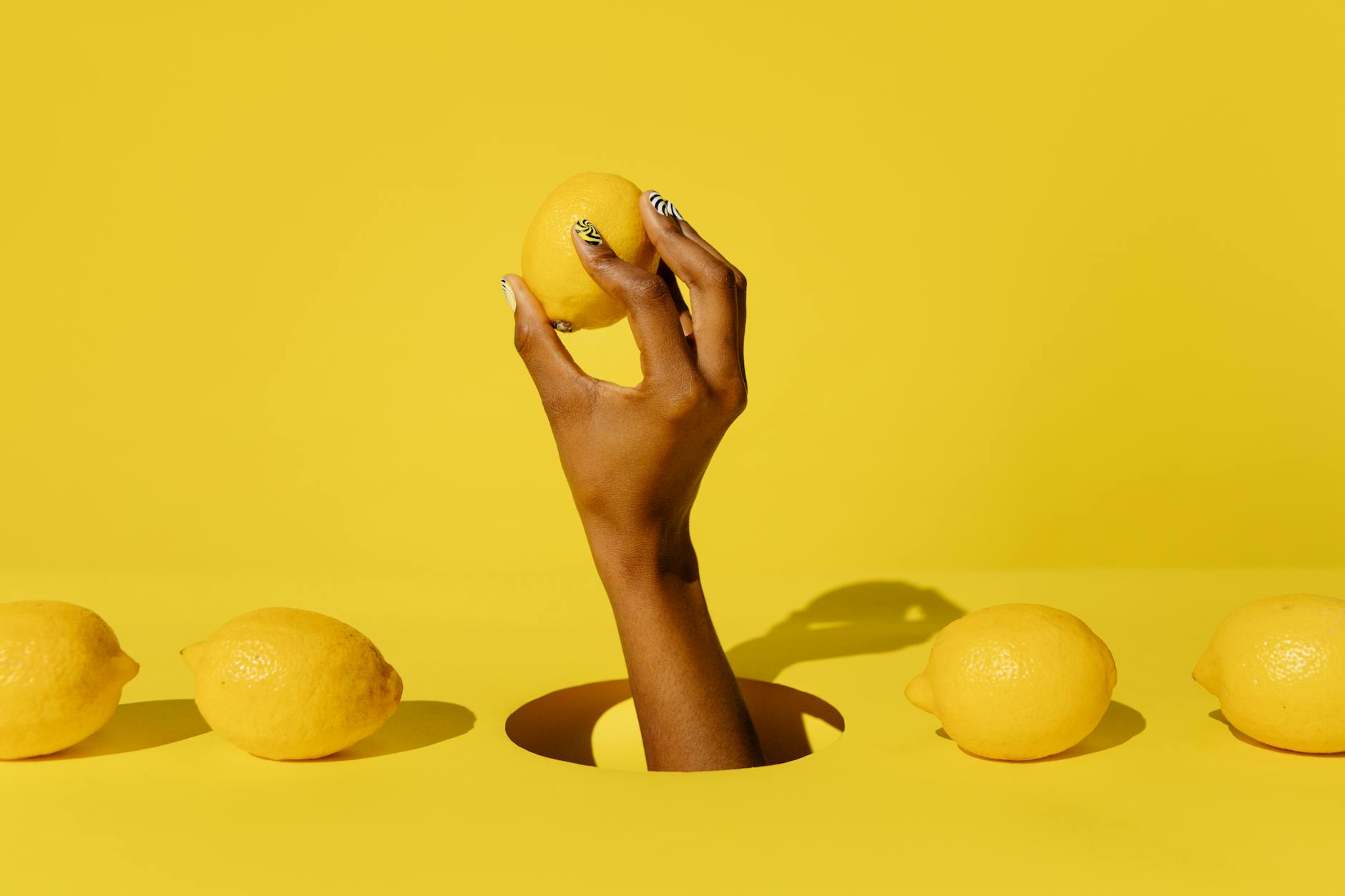 Hand holding a fresh lemon against a bright yellow background, symbolizing the simplicity and joy of starting something new