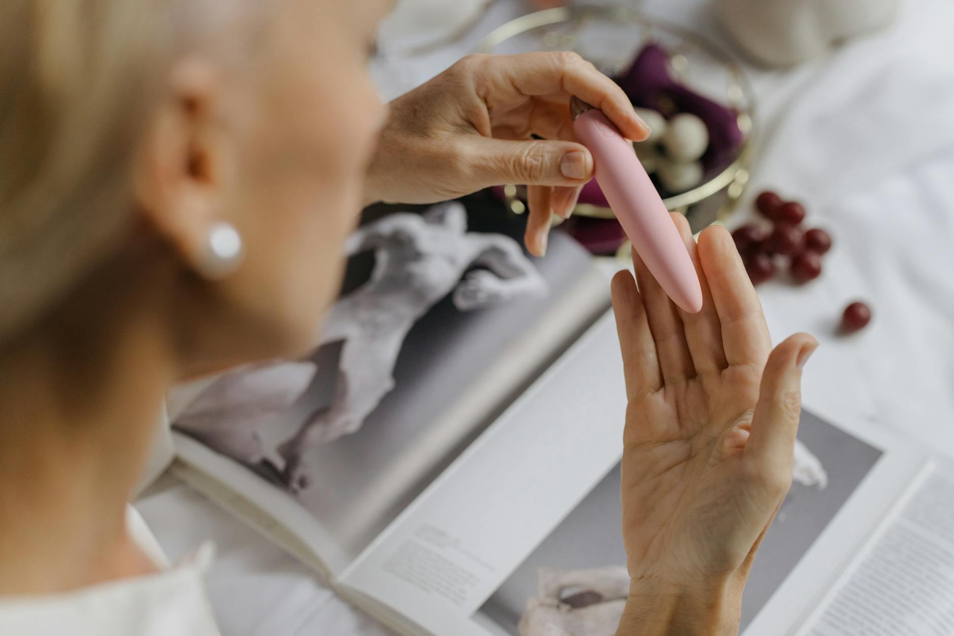 Close-up of a woman holding a pink vibrator with art books in the background, emphasizing intimate and personal reconnection.