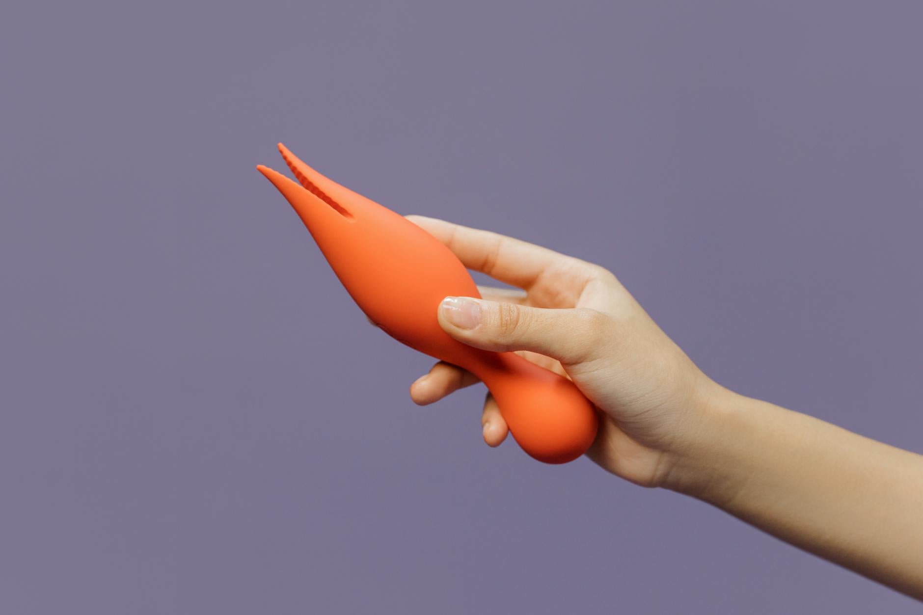Close-up of a hand holding a lemon vibrator against a minimalist purple backdrop