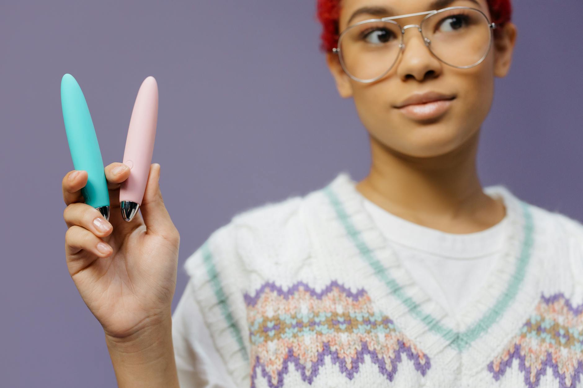 A woman holding two colorful clitoral vibrators against a purple background, representing beginner-friendly lemon vibrators