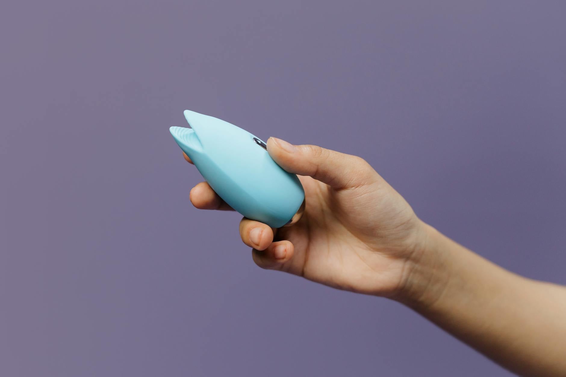 A lemon clitoral vibrator held in hand against a purple background, symbolizing personal pleasure and self-care in long-distance relationships.