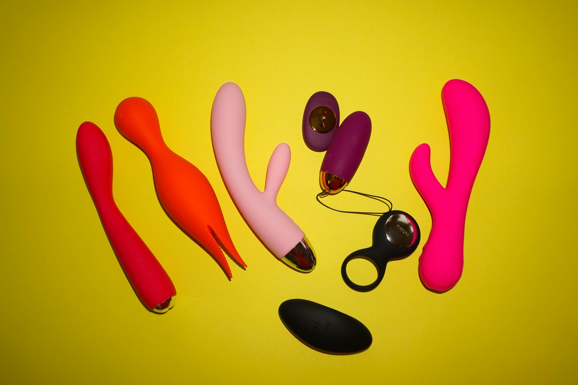 Colorful vibrators and adult toys arranged on a bright yellow background, showcasing various textures and designs