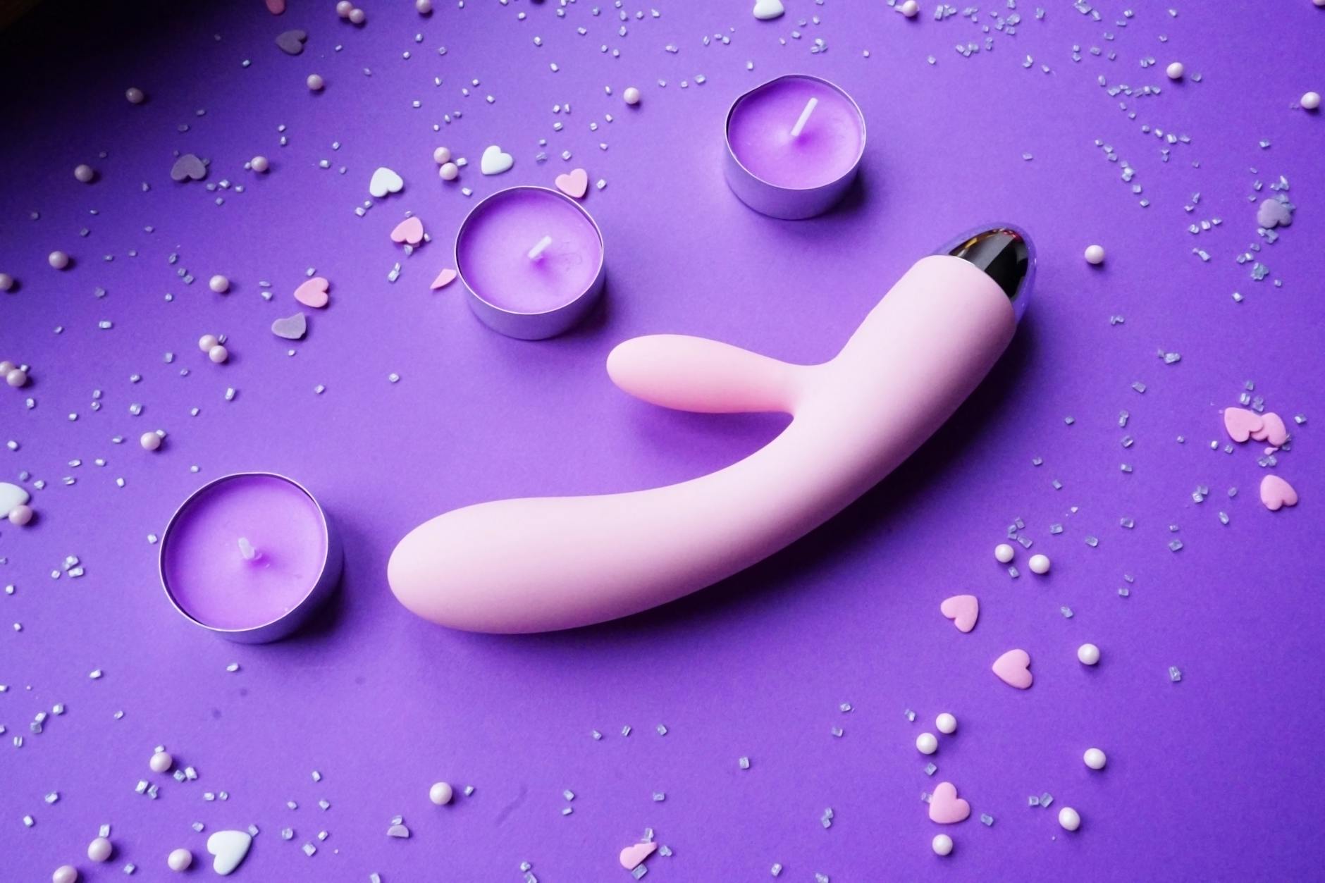 Pink vibrator surrounded by heart confetti and candles on a purple background, suggesting a calm, intentional first experience